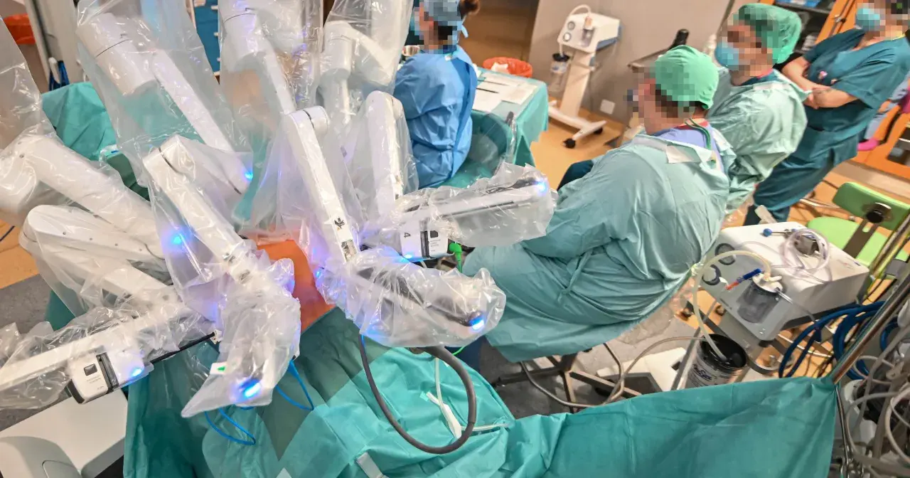 Chirurdzy w zielonych fartuchach prowadzą operację prostaty da Vinci. Robotyczne ramiona systemu są widoczne, pokryte sterylnymi osłonami.