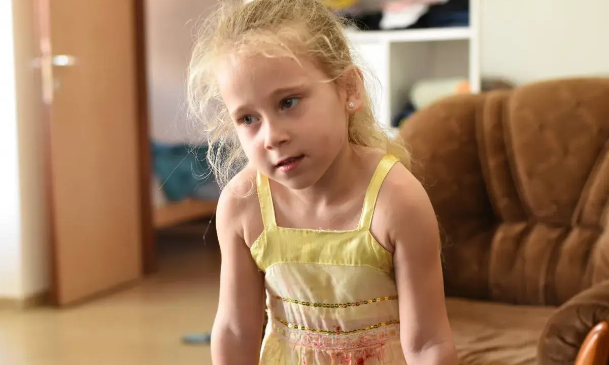 Zmartwiona dziewczynka w żółtej sukience. Co zrobić, gdy dziecko wstrzymuje mocz? Porady dla rodziców.