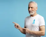 Starszy pan z niebieską wstążką na piersi, wskazujący palcami w lewo. To symbol walki z rakiem prostaty, ważnym tematem dla każdego psa 8.