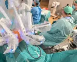 Chirurdzy w zielonych fartuchach prowadzą operację prostaty da Vinci. Robotyczne ramiona systemu są widoczne, pokryte sterylnymi osłonami.