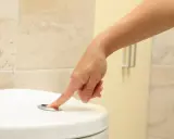 Dłoń naciska przycisk spłuczki. Czasem to prosty sposób, jak pobudzić oddawanie moczu, gdy czujesz potrzebę.