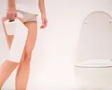 Kobieta z rolką papieru toaletowego obok sedesu. Szuka leków na częste oddawanie moczu w nocy.