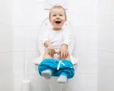 Uśmiechnięte dziecko na sedesie, z opuszczonymi spodniami. Może to być oznaka częstomoczu u dziecka bez innych objawów.