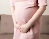 Kobieta w ciąży w różowej sukience trzyma ręce na brzuchu, doświadczając dyskomfortu związanego z nietrzymaniem moczu w ciąży.