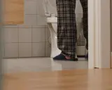 Nocne parcie na pęcherz w pozycji leżącej. Osoba w piżamie i kapciach stoi przy toalecie.