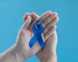 Dłonie trzymające niebieską wstążkę symbolizującą wsparcie dla mężczyzn. Warto poznać domowe sposoby na prostatę.