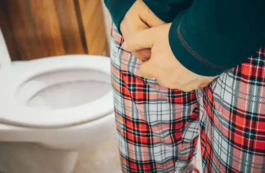 Osoba w piżamie w kratę przy toalecie, odczuwająca jednoczesne parcie na mocz i stolec.