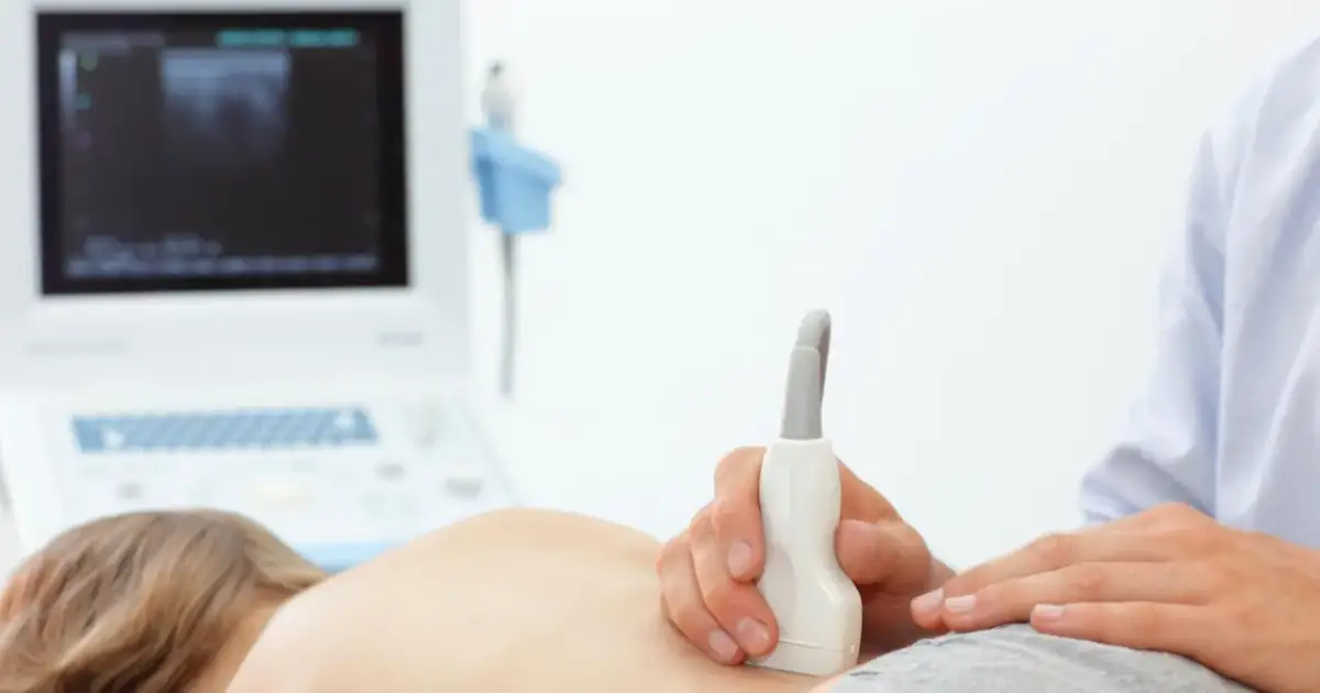 Badanie USG nerek u dziecka, które może pomóc zdiagnozować zapalenie nerek. Lekarz przykłada sondę do pleców pacjenta.