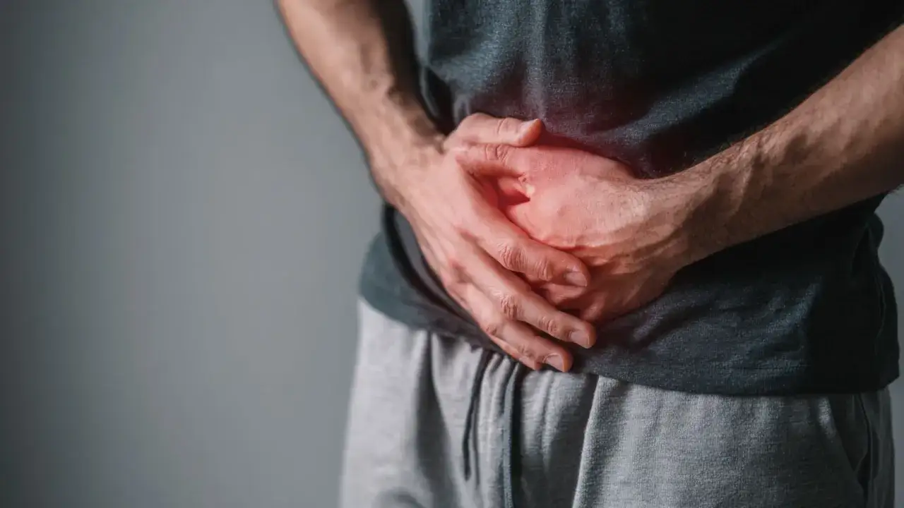 Mężczyzna trzyma się za podbrzusze, odczuwając ból. Szuka domowych sposobów na prostatę.