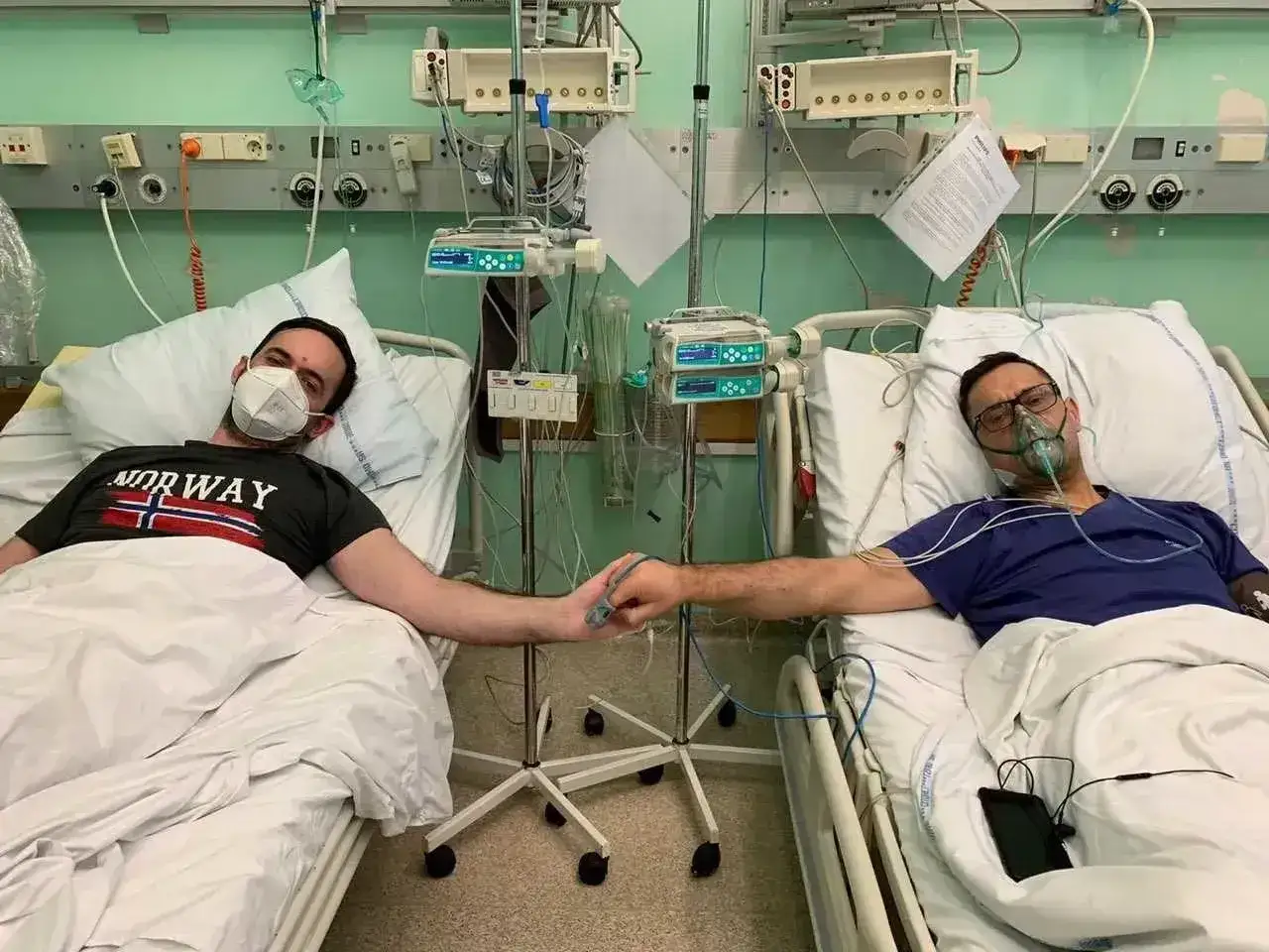 Dwóch pacjentów w szpitalnych łóżkach, podłączonych do aparatury, trzyma się za ręce. Jeden z nich ma maskę tlenową, drugi maseczkę. Może to być obraz dolegliwości po usunięciu nerki.