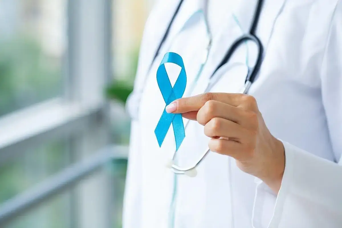 Lekarz trzyma niebieską wstążkę symbolizującą walkę z rakiem prostaty. Rozmiar guza jest kluczowy w diagnostyce.